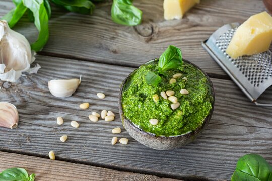 Green pesto in a glass jar made from fresh basil leaves, pine nuts, parmesan, garlic and olive olia on a wooden background. Popular Italian dressing for salads, pasta and pizza.