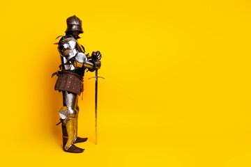 Medieval knight in armor with sword posing on yellow backdrop, blending historical style with modern art