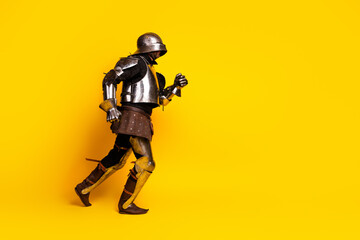 Medieval knight in full metal armor walking against a vibrant yellow background, showcasing historical fashion and style