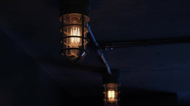 Two industrial lights on a ceiling flicker during a power outage.  	