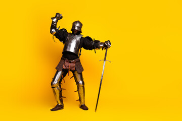 Young man dressed in medieval knight's armor striking a heroic pose against a vibrant yellow background