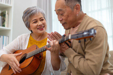 Happy asian senior elderly couple take it easy on retirement holidays playing guitar having fun in living room at home, Happiness singing together. Taking care of each other health in old age.