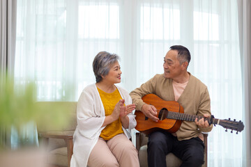 Happy asian senior elderly couple take it easy on retirement holidays playing guitar having fun in...