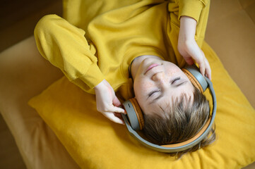 A boy lying down and listening to music with headphones on. He is relaxed and immersed in the music, enjoying a peaceful moment. The setting is comfortable, possibly indoors, with a calm and cozy atm