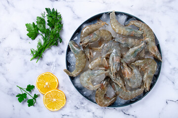 Fresh raw shrimp spread on ice with lemon and cilantro slices on a marble surface, ready to cook, no people
