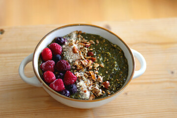 Beige bowl with green smoothie, frozen berries and homemade granola, served on the table. Selective focus.