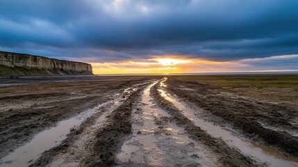 Muddy trails and scenic adventures. Muddy tracks lead to a dramatic sunset over a coastal landscape.