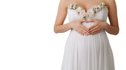 Expecting mother in a beautiful white dress forming a heart shape with her hands on her pregnant belly, surrounded by soft floral decorations.