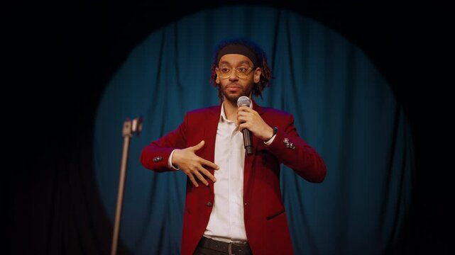 Charismatic male comedian performing stand-up comedy show, portrait on stage. Handsome african american man in red jacket, professional humorist entertaining audience, happy emotional performer