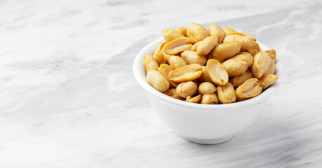 Roasted peanuts in white bowl on marble table