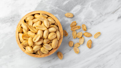 Salted roasted peanuts in wooden bowl on marble table, top view