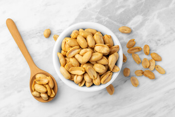 Roasted peanuts in white bowl with wooden spoon on marble table