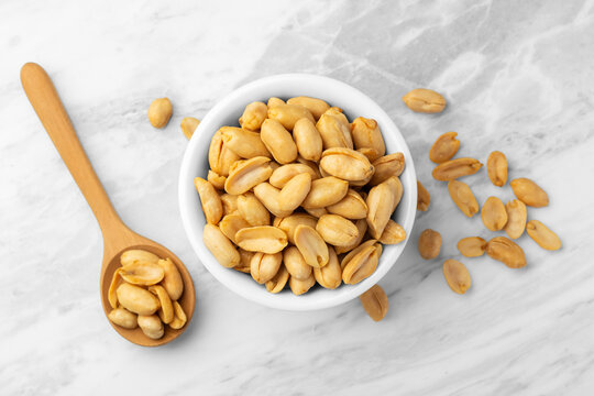 Roasted peanuts in white bowl with wooden spoon on marble table