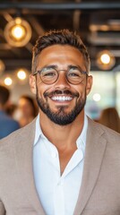 Fototapeta premium Smiling man in a beige blazer and white shirt. He's wearing round glasses and has a beard.