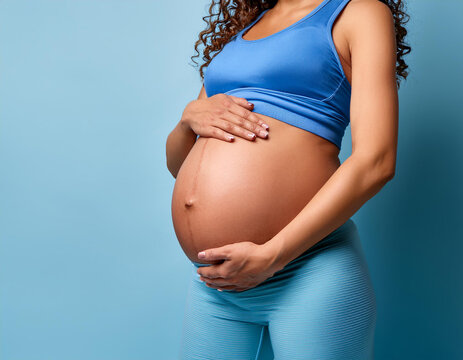 Plano medio de una mujer embarazada con las manos sobre la barriga con ropa deportiva y fondo azul
