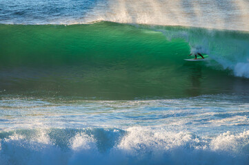 Surfer ridding a wave in Coxos in Ericeira, Portugal. A surfer riding a powerful wave with the spray and ocean in the background.