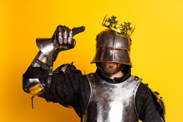Medieval knight in royal crown posing against bright yellow background portraying bravery and...