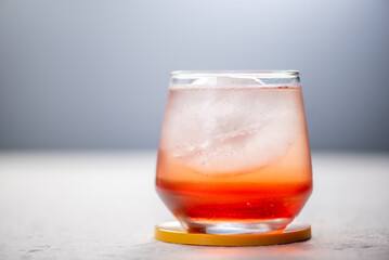 Closeup of a hand pouring sparkling water into a glass with red liquid and ice.