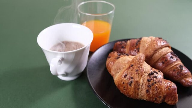 Piatto con cornetti, bicchiere di spremuta d'arancia e tazza con caff&egrave; caldo fumante