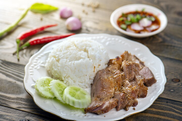 A plate of rice, grilled pork, cucumber slices, and a bowl of dipping sauce.