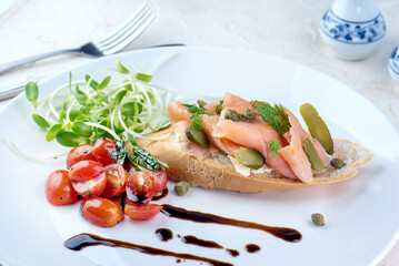 A plate of smoked salmon and cream cheese crostini with pickled cucumbers, cherry tomatoes, and balsamic glaze.