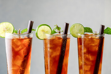 colorful cool ice tea lemonade cocktails in glasses with straw on gray background. Mix glass of...