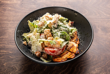 A fresh and colorful Caesar salad in a black bowl, featuring crisp romaine lettuce, grilled chicken, croutons, and a sprinkle of Parmesan cheese