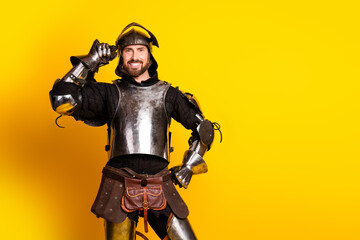 Handsome young man dressed in medieval knight armor posing against a vibrant yellow background...