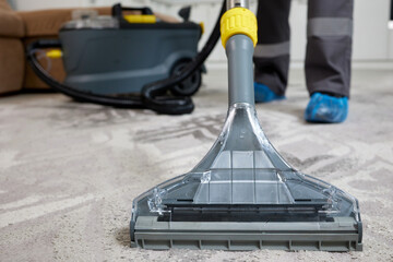 A cleaner from a professional agency in overalls is meticulously cleaning a carpet in a well-lit...