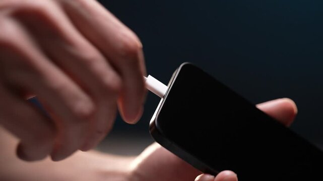Close-up hands of unrecognizable man plugging charging cable into phone and unplugging it, repeating action multiple times standing on black background. Concept of contemporary technology convenience.