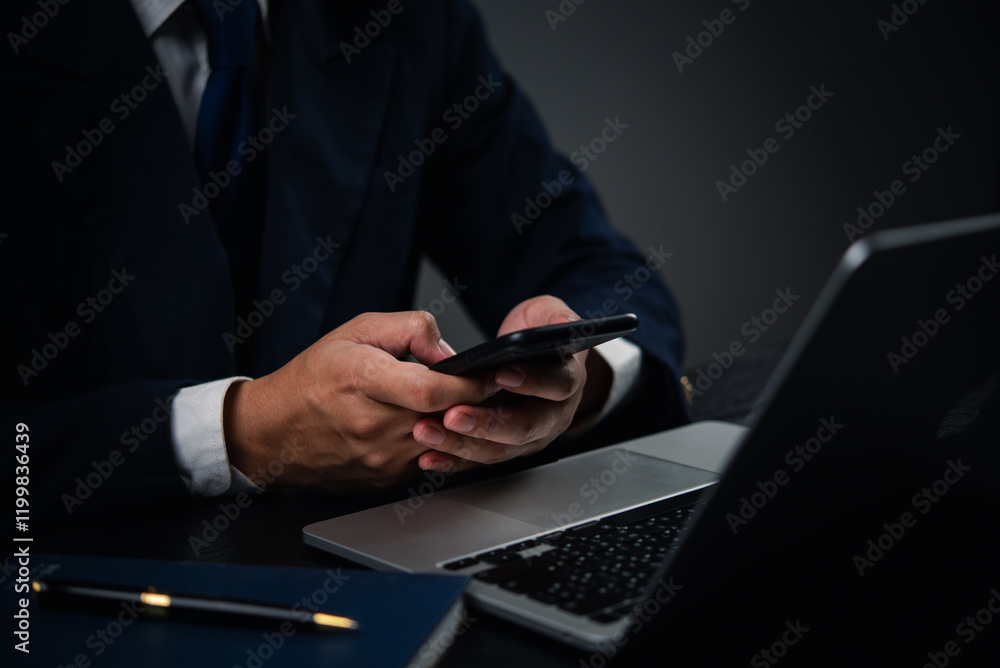 Poster man holding a smartphone while typing on a laptop keyboard in an office or home setting, representin