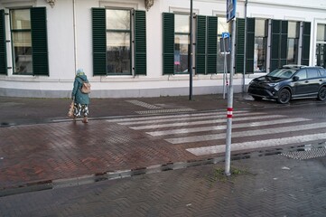 A woman in colourful clothes and with backpack crosses a crosswalk in the rain.