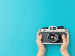 A pair of hands holding a vintage camera against a bright turquoise background, symbolizing the joy of photography and creative expression.