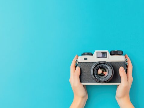 A pair of hands holding a vintage camera against a bright turquoise background, symbolizing the joy of photography and creative expression. - Powered by Adobe