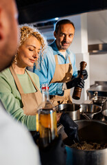 Couple enjoying a cooking class with a chef preparing meal in the kitchen.