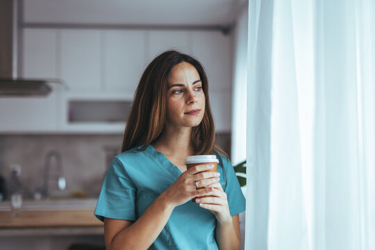 Thoughtful Nurse Relaxing With Coffee at Home Near Window