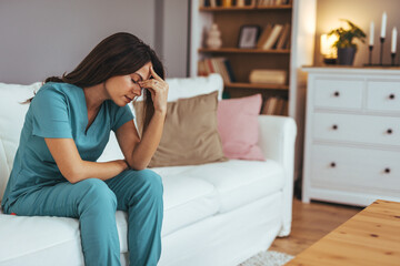 Obraz premium Tired Medical Professional Sitting on Sofa Feeling Stressed in Living Room