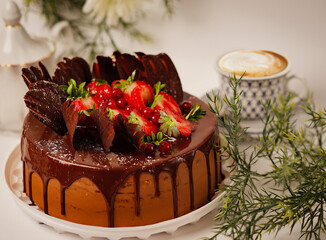Elegant chocolate cake topped with fresh strawberries, red currants, and decorative chocolate...