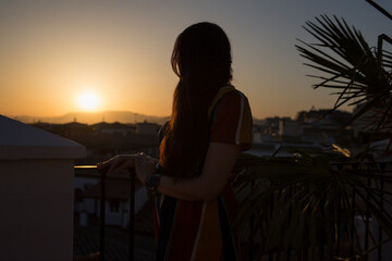 Silhouette of a woman looking out from a balcony in Granada, Spain. In the background is the sunset.