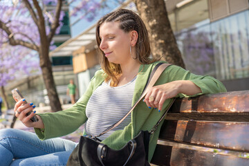 Fototapeta premium Woman sitting on a park bench using her smartphone on a sunny day.