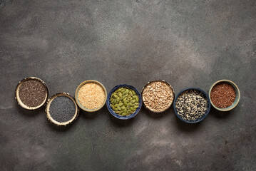 Various seeds in bowls in a row on a dark rustic background, top view