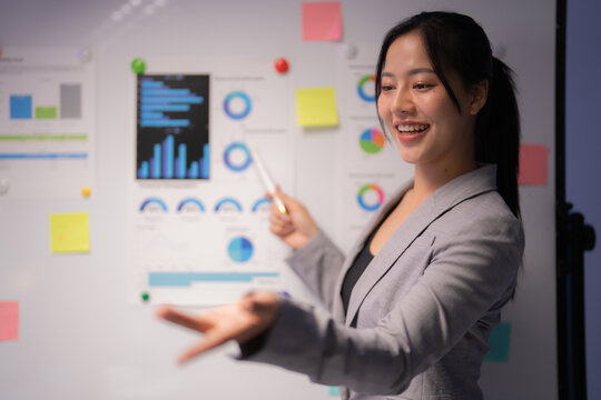 Young professional woman engaging in a business meeting, explaining company strategy while pointing at charts and smiling, showcasing confidence and leadership in the corporate environment