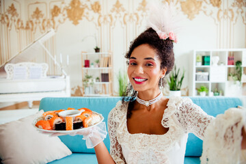 Elegant woman in vintage aristocratic attire holding a sushi platter indoors
