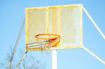Naklejka premium A red hoop on a white rusty metal backboard on a basketball court in a public park.