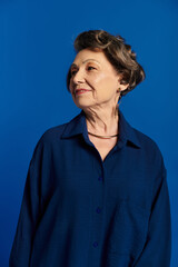 A beautiful woman in her 60s showcases her style and confidence against a vivid blue background.