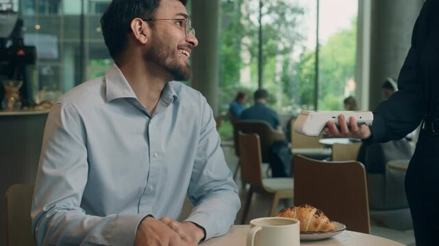 Waiter serving visitor in cafe Indian man guy male customer buyer client businessman coffee pay smartphone wifi scan contactless NFC payment online technology mobile phone credit card bank terminal