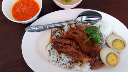 Top view of Stewed pork leg with boiled egg on rice with sour sauce and sweet soup on wooden background. Thai or famous food in Tbailand on wood table.