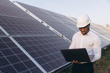 African American Engineer Inspecting Solar Panels With Laptop in Solar Farm