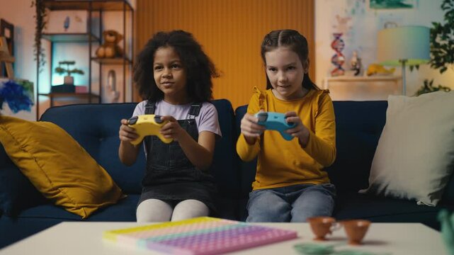 Two little girls play a video game at home, giving high fives in celebration