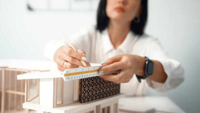 Closeup portrait image of professional young beautiful engineer architect using triangular scale measures house model with focusing at modern office. Business creative design concept. Immaculate.